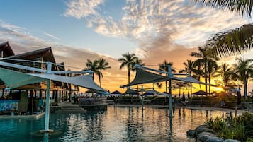 Ein Poolbereich eines Resorts mit Sonnenuntergangsblick, Palmen und schattigen Sitzbereichen.