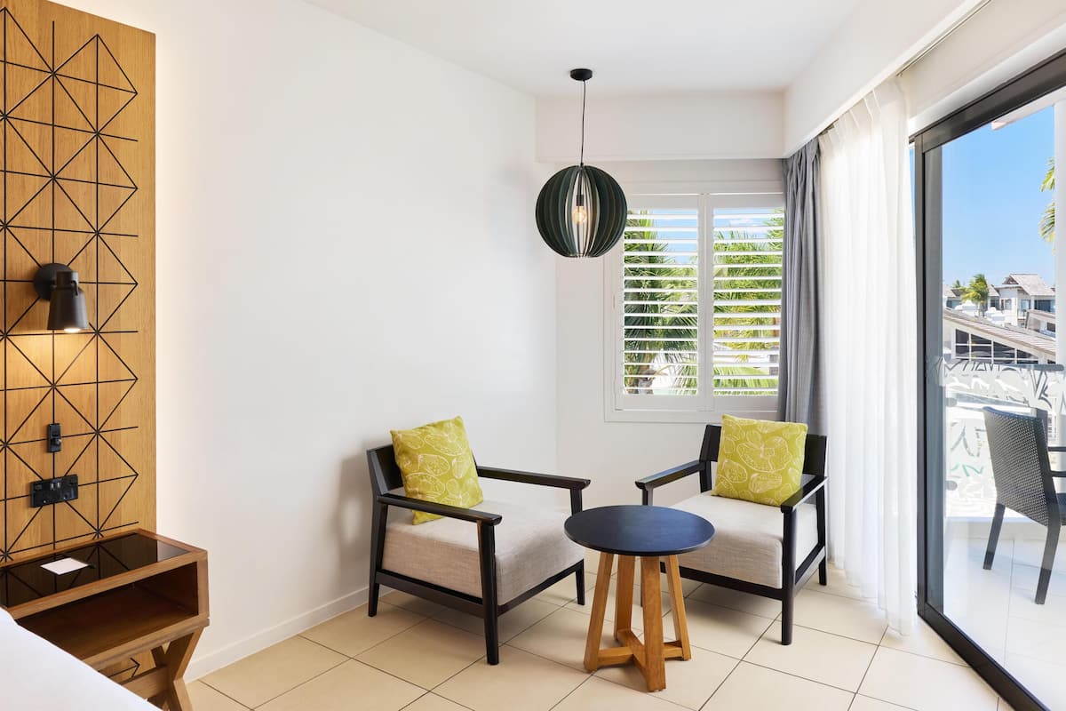 A modern room with two chairs, a small table, a geometric wall design, and a large window with blinds.