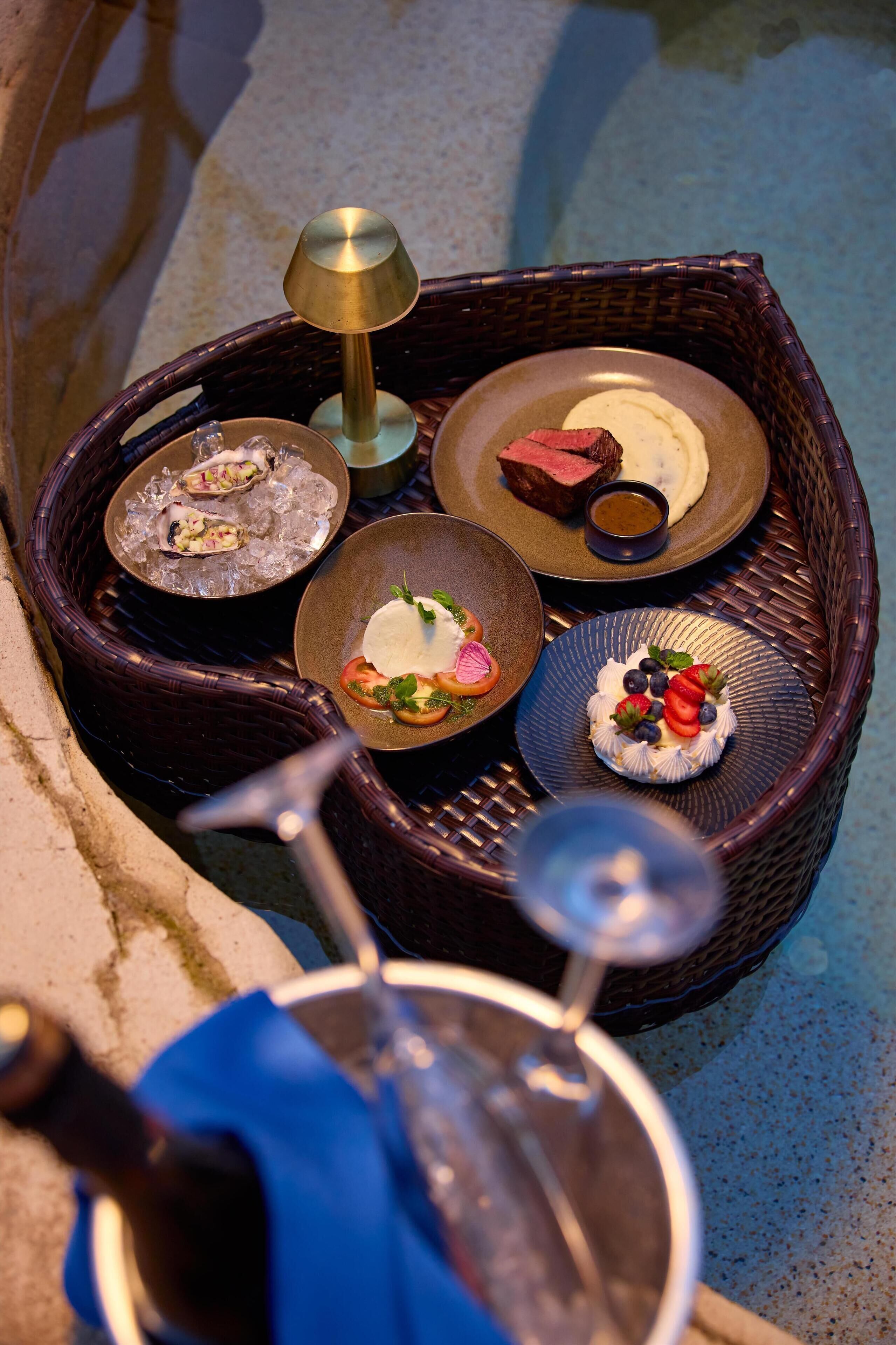 A wicker basket with various dishes, including seafood and a steak, and a wine bottle.