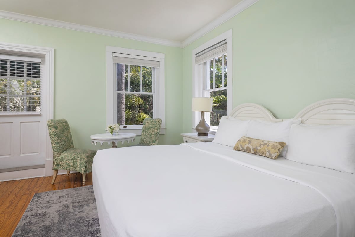 A bedroom with a large bed, a chair, a small table, and a window with blinds.