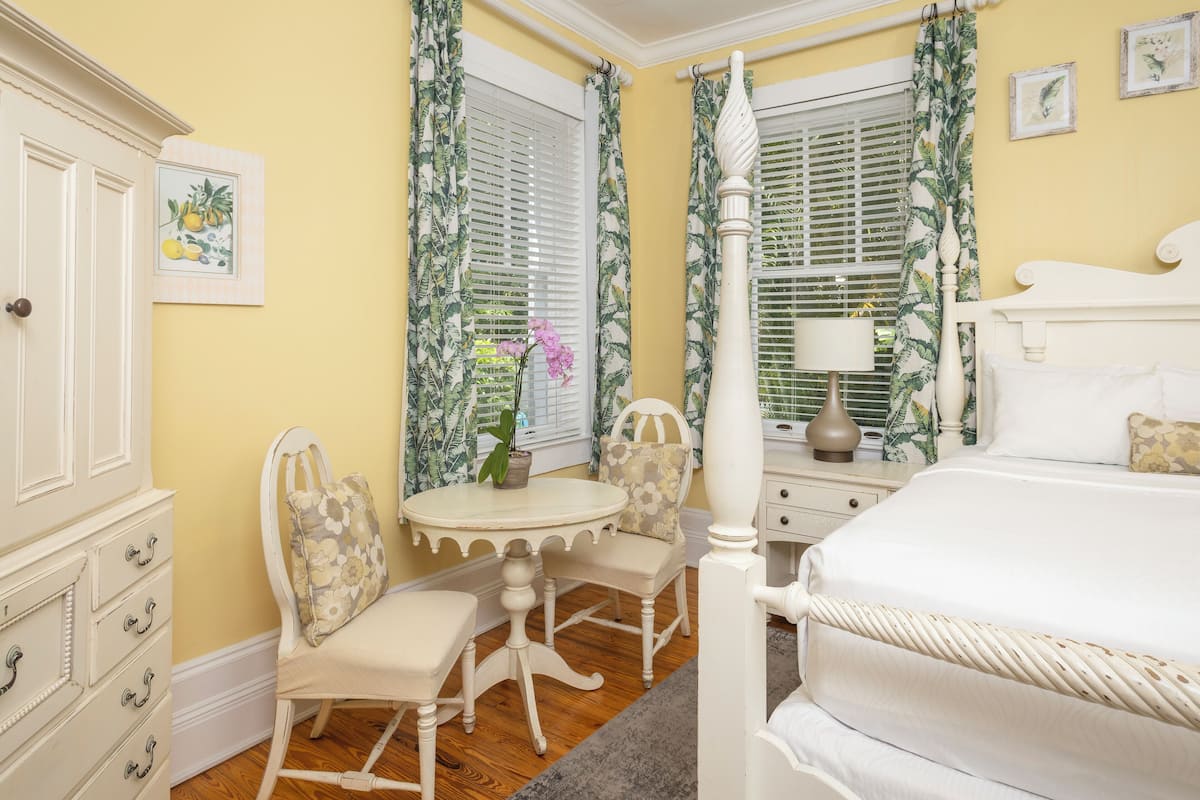 A bedroom with a bed, a nightstand, a chair, a table, and a dresser.