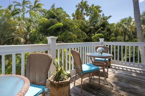 A wooden deck with wicker furniture and a white railing, surrounded by lush tropical vegetation.