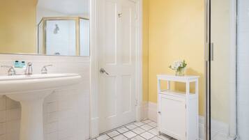 Une salle de bain avec un lavabo blanc, une porte, un petit meuble blanc et un espace douche.