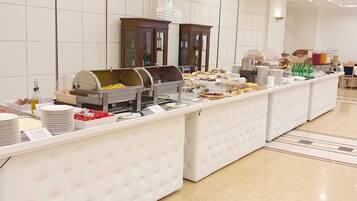 Disposição de buffet com diversos alimentos e bebidas, uma parede revestida de azulejos e um armário de madeira ao fundo.