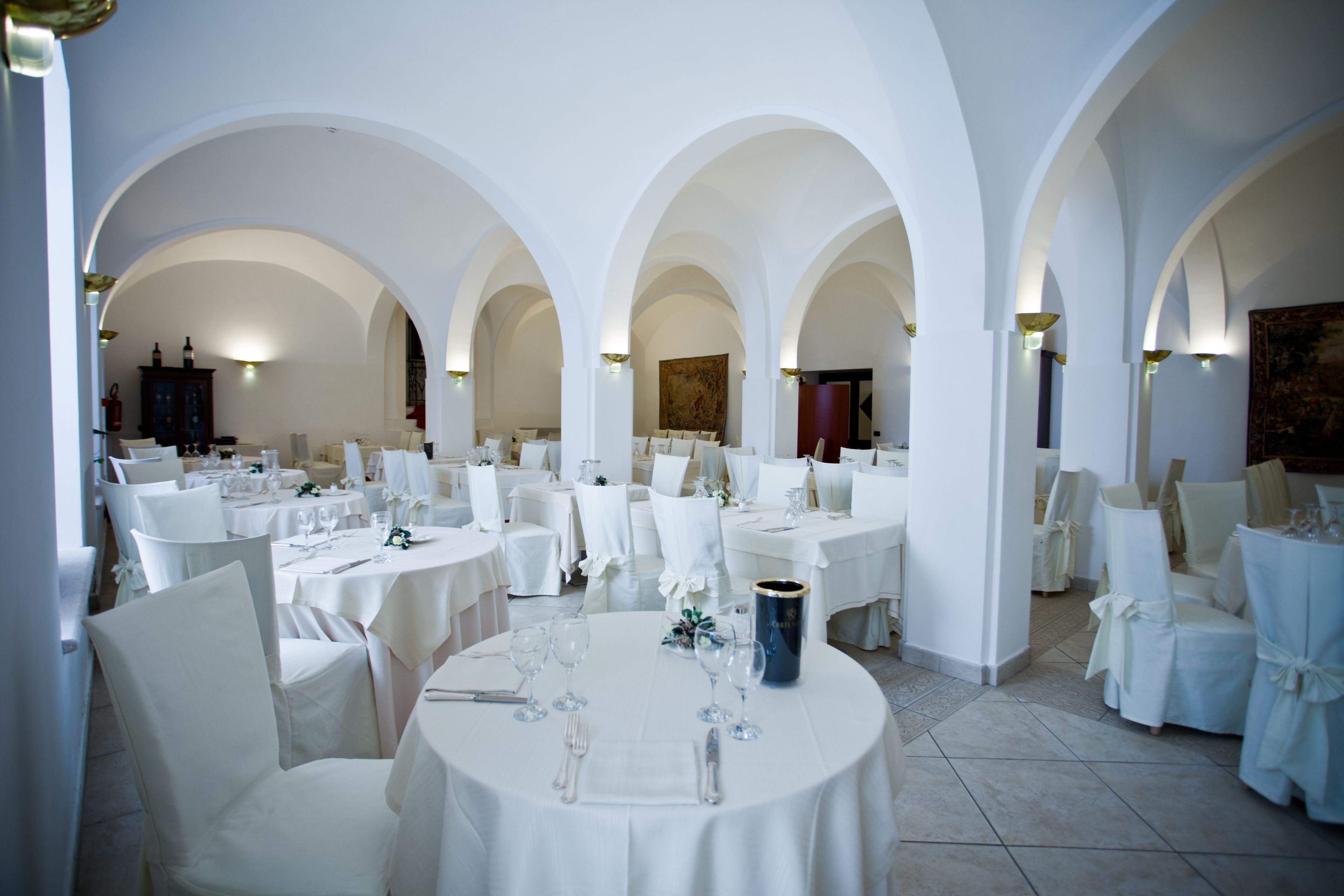 A spacious dining area with multiple round tables, white chairs, and arches.