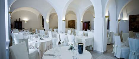 A spacious dining area with multiple round tables, white chairs, and arches.