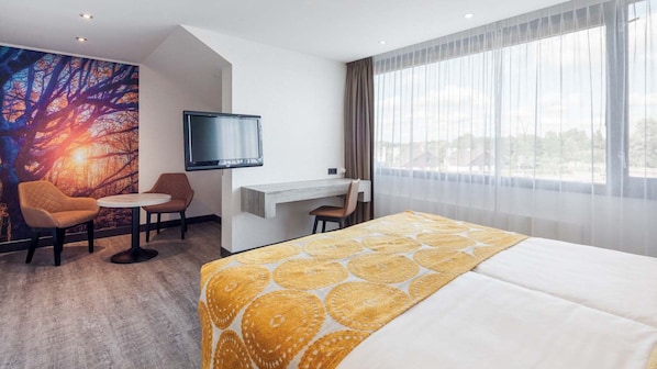A hotel room with a bed, a desk, a chair, a television, and a large window with curtains.