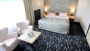 A hotel room with a bed, two bedside tables, a TV, a small table with a magazine, and two chairs.