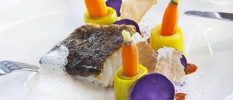 A white plate with a piece of fish, carrot, and purple vegetable garnish.
