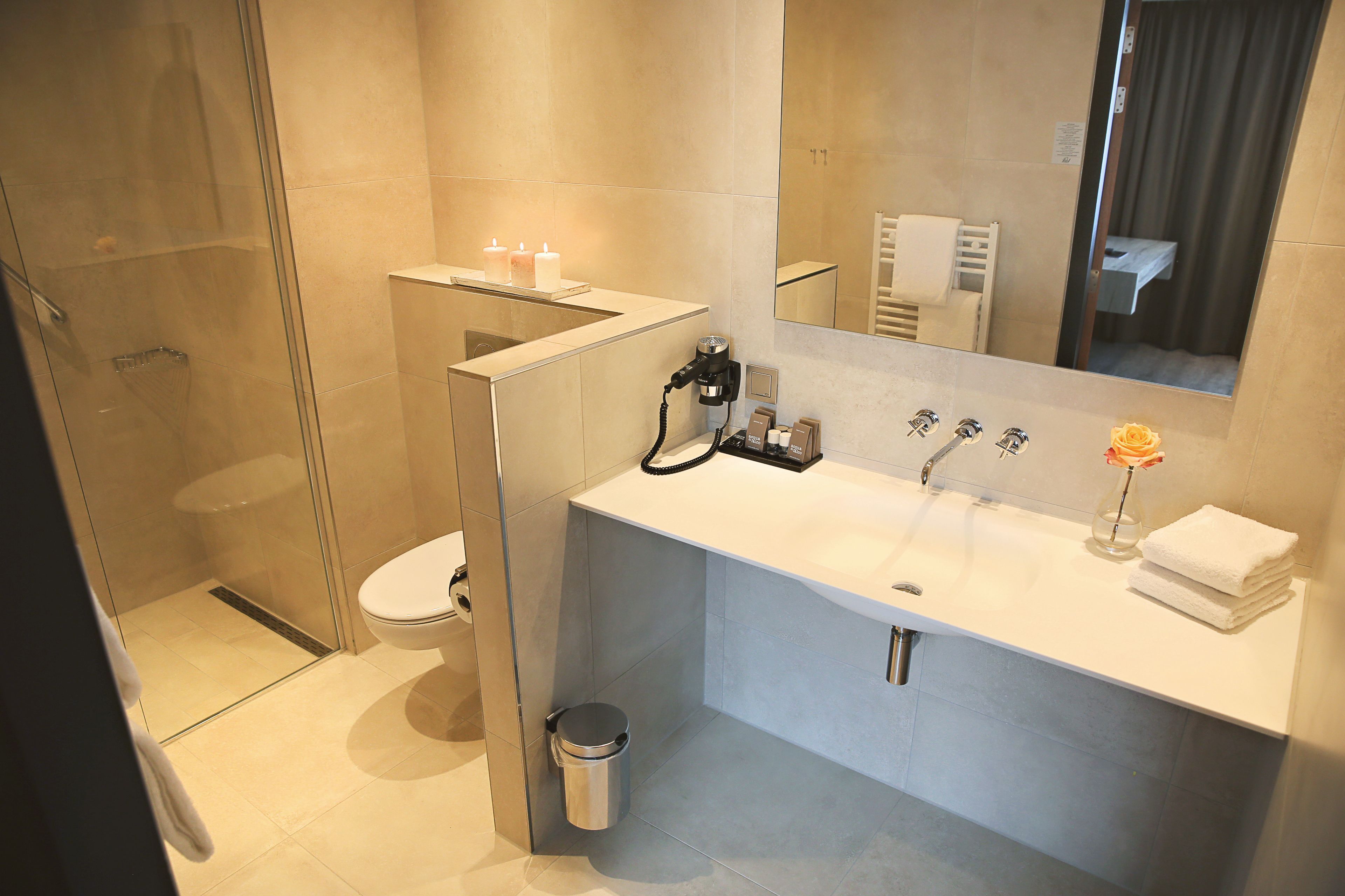 A modern bathroom with a glass shower enclosure, a white sink with a mirror above it, and a small trash bin.