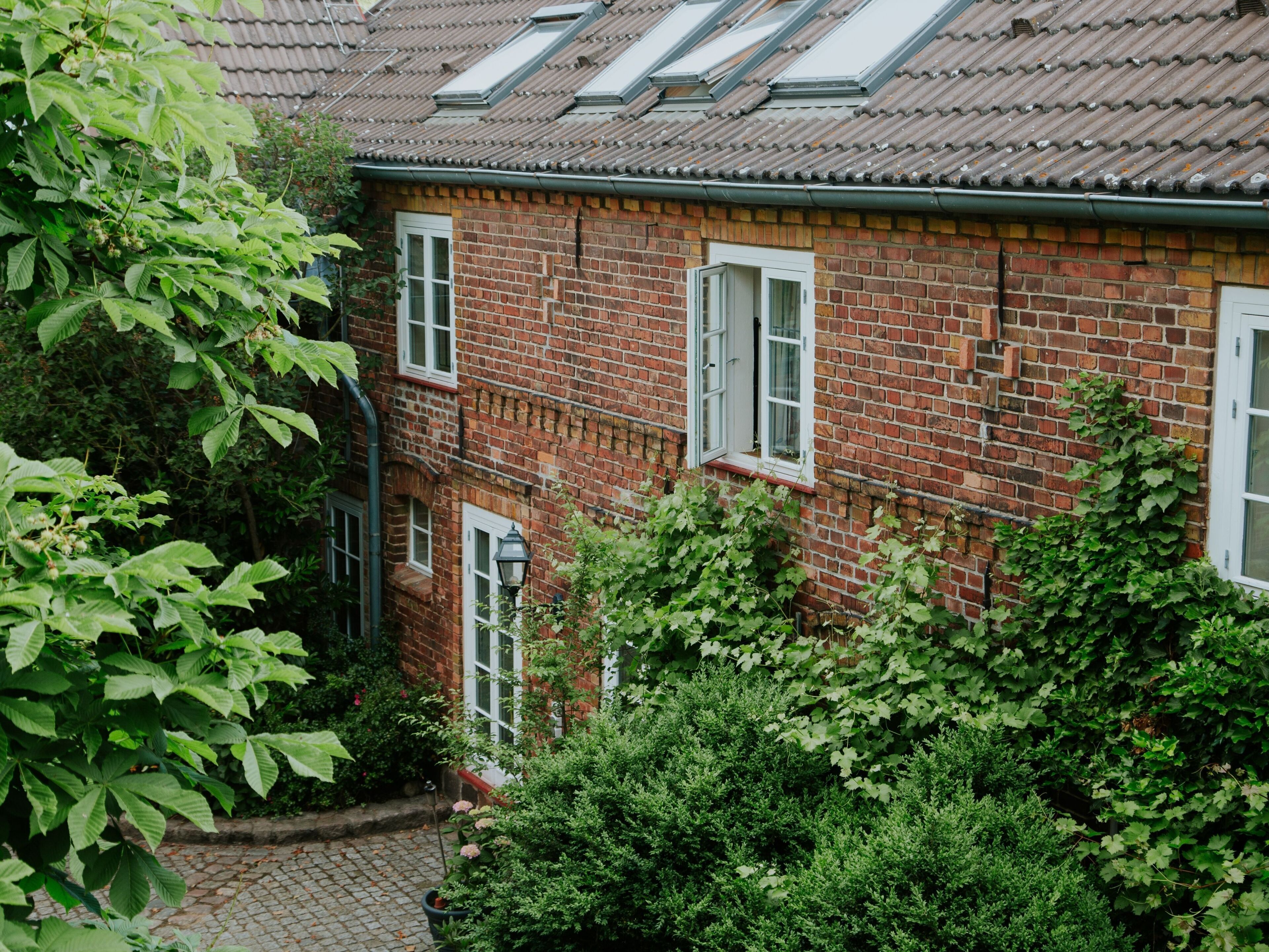 A red brick building with white-framed windows, a visible chimney, and a brick pathway leading to the entrance.