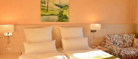 Habitación de hotel con cama doble, dos lámparas de noche, un sofá floral y un cuadro de un paisaje en la pared.