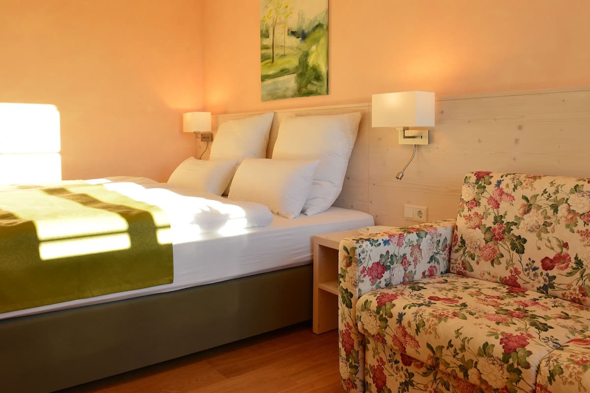 Une chambre d’hôtel avec un lit, une table de chevet, un fauteuil à motifs floraux et un tableau au mur.