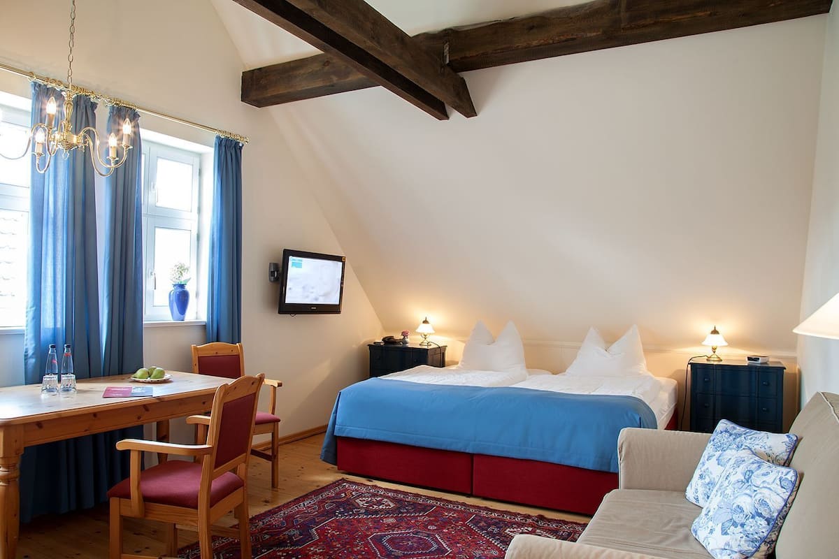 Une chambre à coucher comprenant un lit, des tables de chevet, un bureau, une chaise, un téléviseur et une fenêtre avec des rideaux.