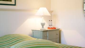 A neatly made bed with striped bedding, a bedside table with a lamp, and a small tray with bottles and glasses.