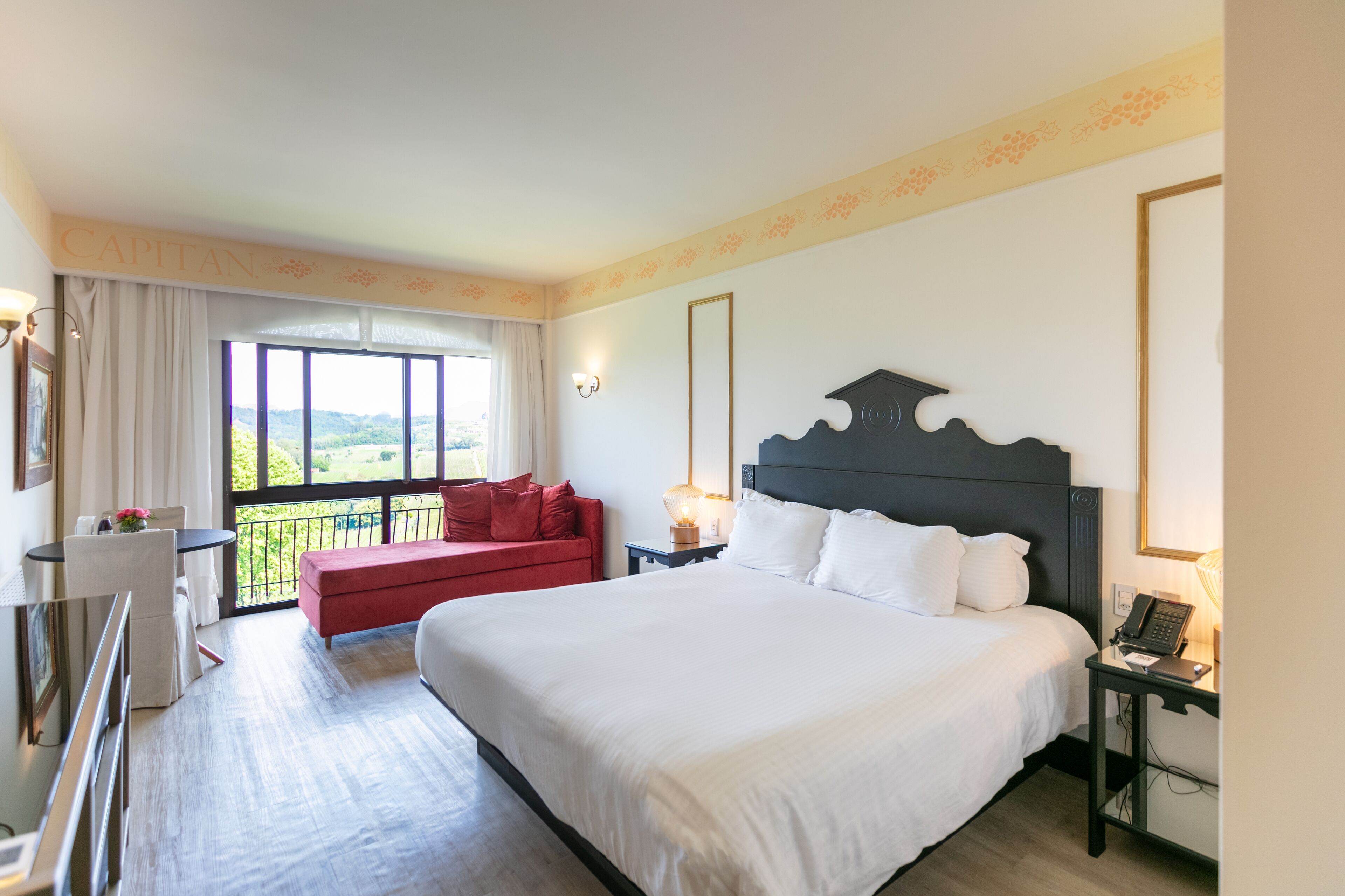 Habitación de hotel con una cama grande, un sofá rojo, una mesita y un balcón con vistas.