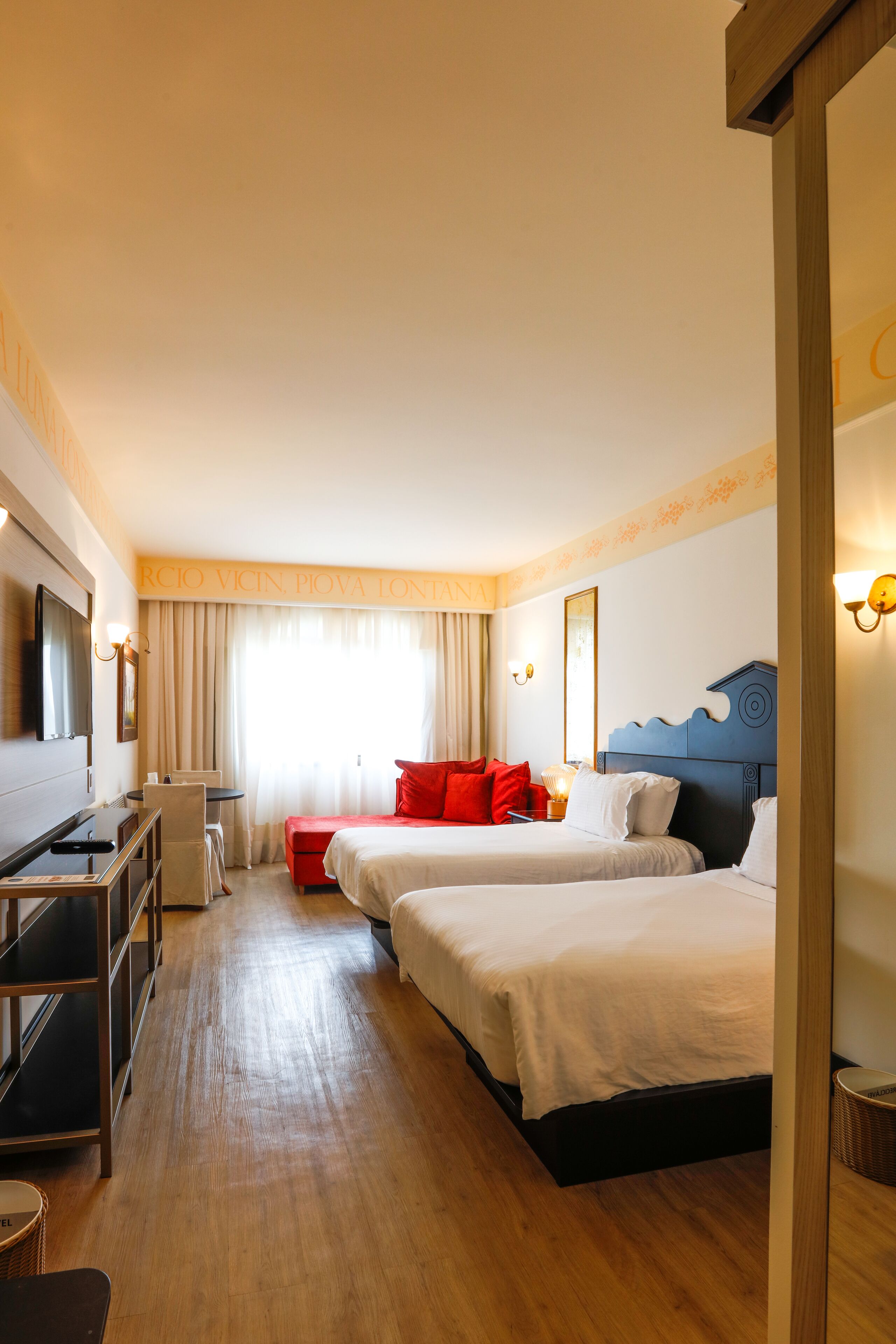 Une chambre d’hôtel avec deux lits, un bureau, une chaise, une télévision et une fenêtre avec des rideaux.