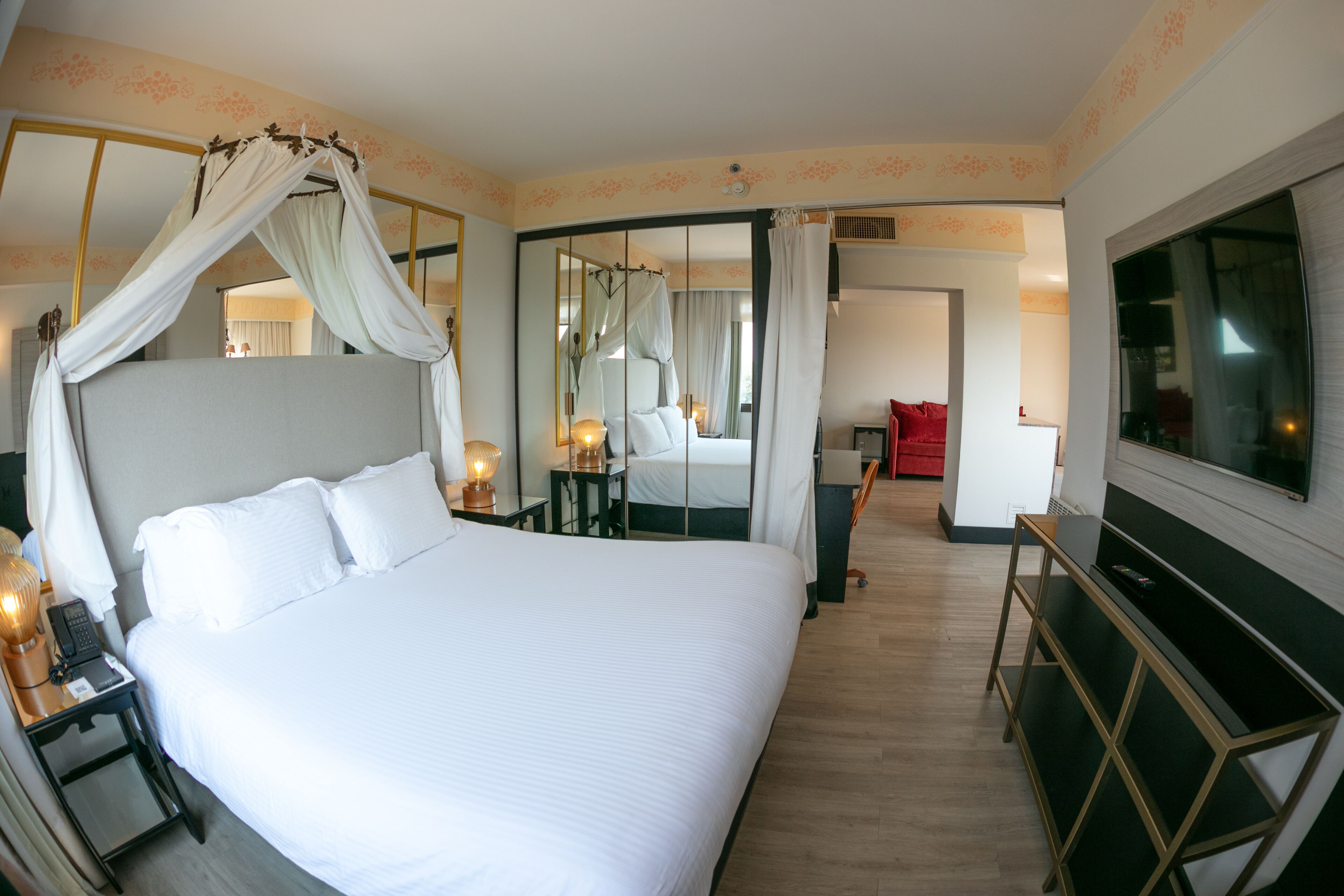Een groot bed met hemelbed, nachtkastjes met lampen, een televisie en een spiegel.
