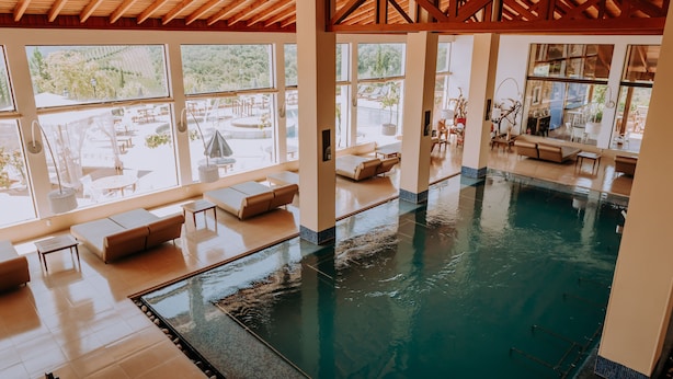 An indoor swimming pool with a view of the outdoors, surrounded by lounge areas and large windows. - Spa do Vinho Hotel & Condomínio Vitivinícola (Bento Gonçalves)