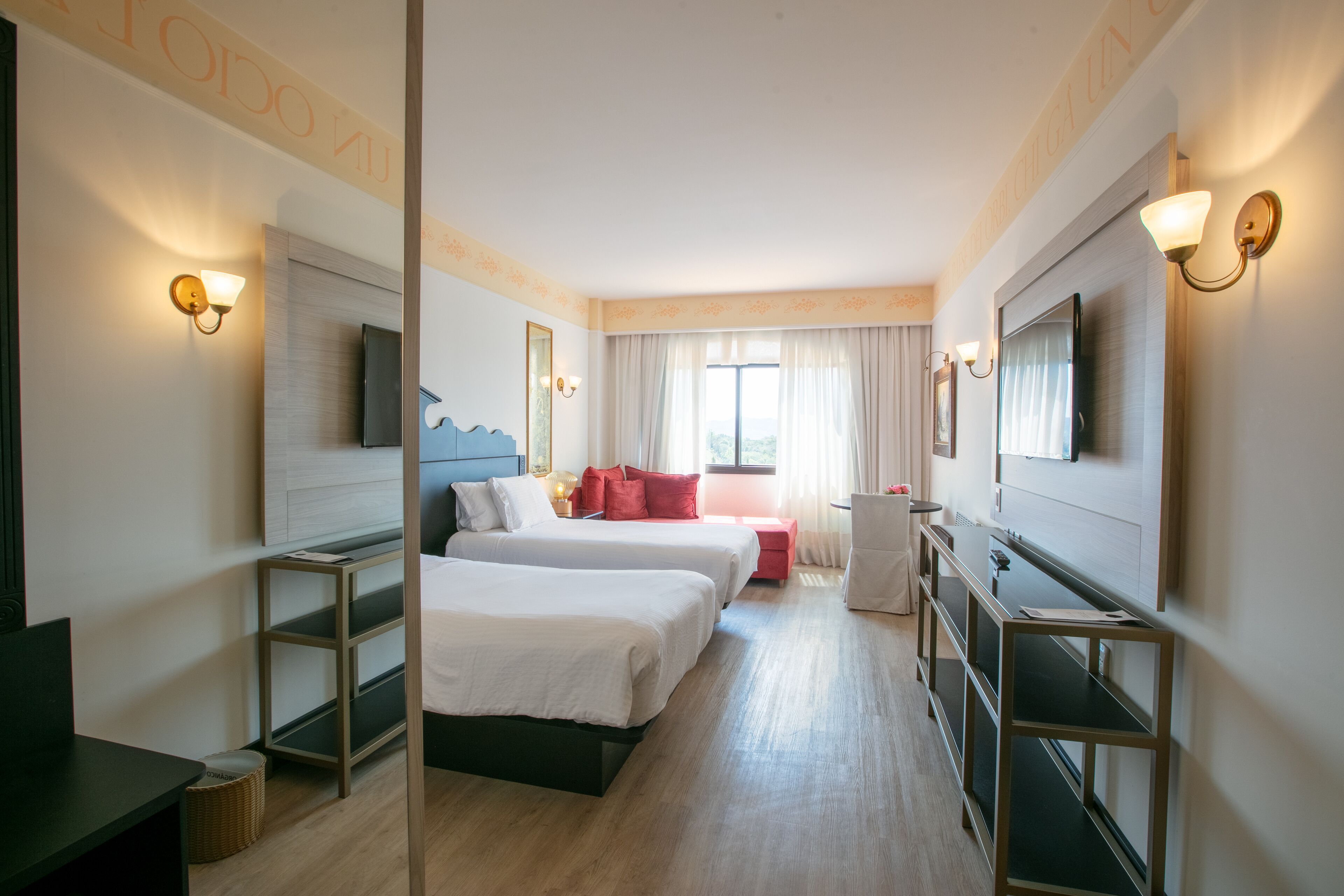 A hotel room with two beds, a TV, a desk, and a window with curtains.