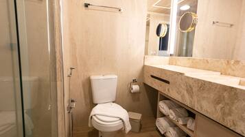 A bathroom with a glass-enclosed shower, a toilet, a sink with a marble countertop, and a mirror above the sink.