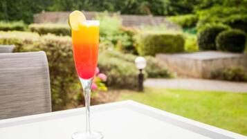 A clear glass with a gradient drink, a slice of lime, and a white table in a garden setting.