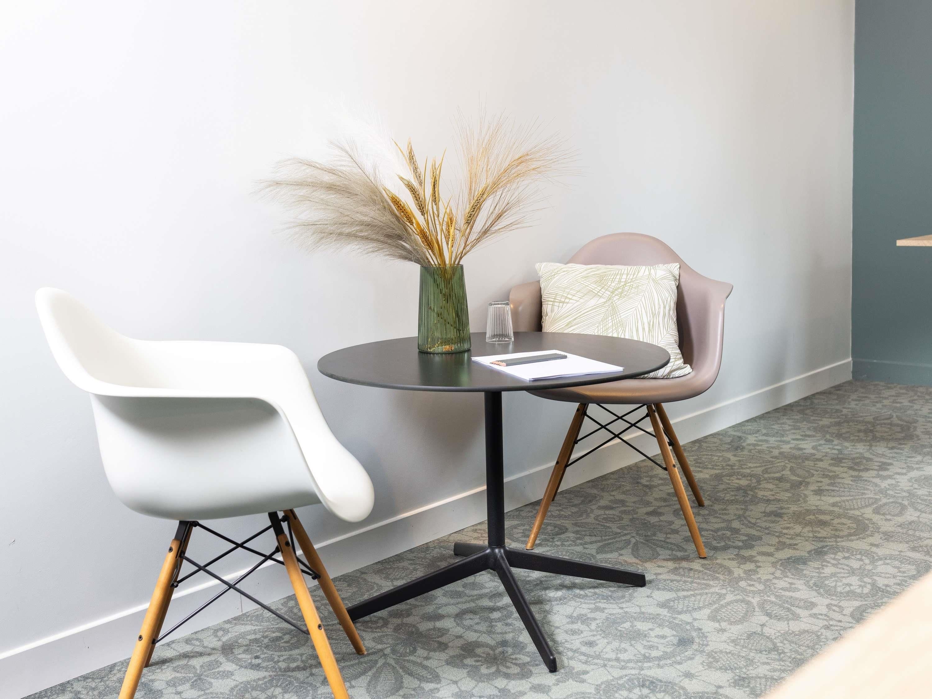 Ein modernes Zimmer mit einem runden Tisch, zwei Stühlen, einer Vase mit Trockenpflanzen und einem gemusterten Teppich.