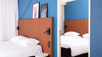 Una habitación de hotel moderna con una cama individual, una mesita de noche redonda y un cabecero con panel de control.