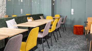 A modern dining area with wooden tables and colorful chairs, a green wall, and a patterned carpet.
