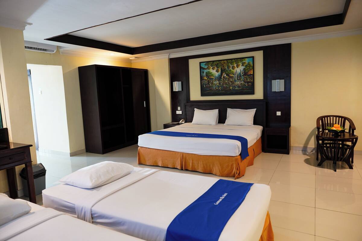 A hotel room with two beds, a wardrobe, a painting on the wall, and a chair with a flower.