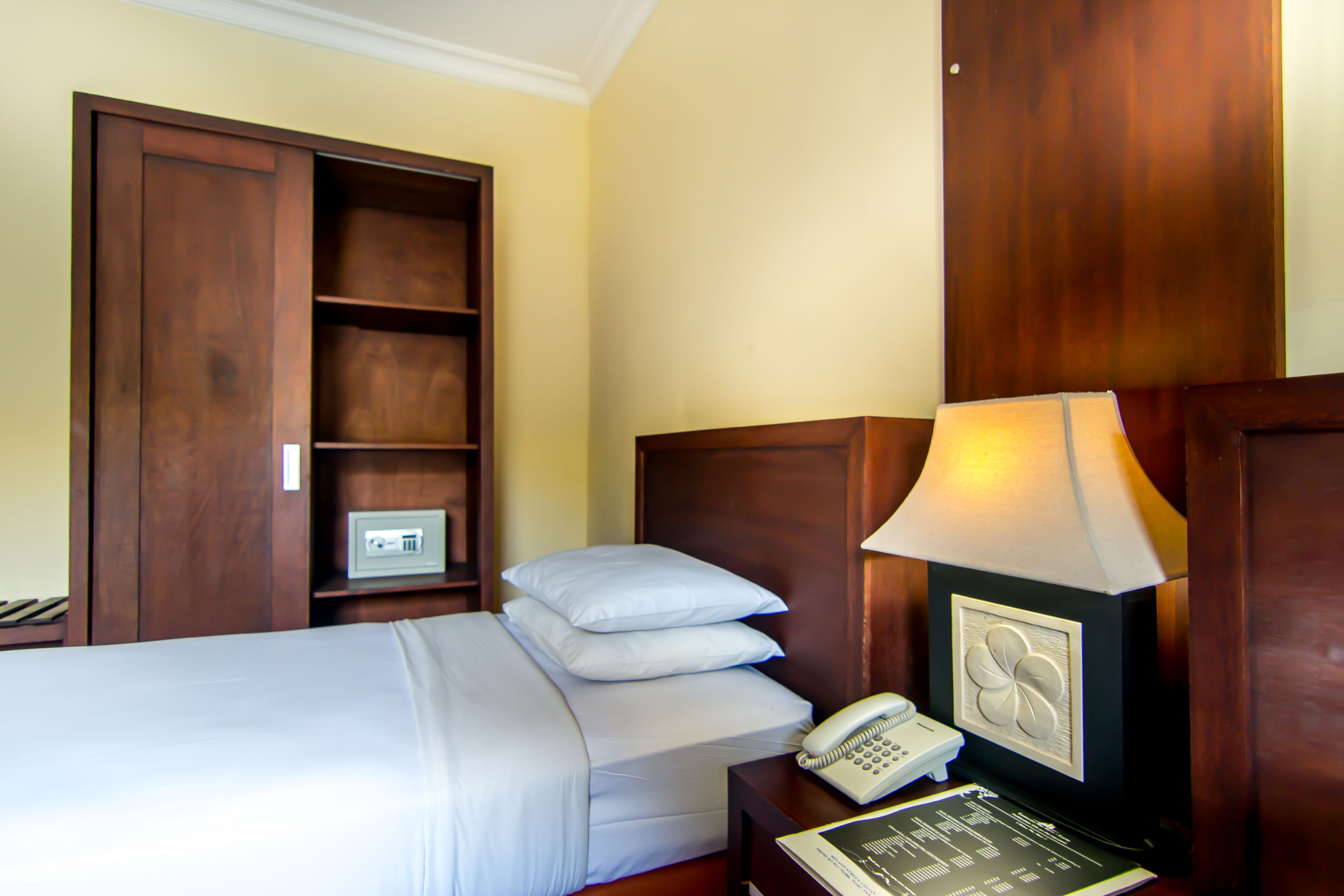 A hotel room with a bed, a bedside table with a lamp, a phone, and a safe.