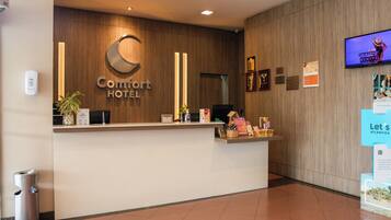 A hotel reception desk with a wooden panel wall, a digital screen, and a trash bin.