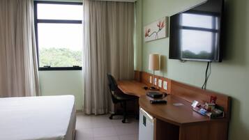 A hotel room with a bed, desk, chair, television, and a window with curtains.