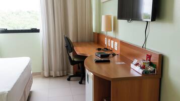 A hotel room with a bed, desk, chair, TV, and window with curtains.