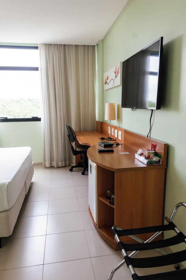 Habitación de hotel con cama, escritorio, silla, televisión y ventana con cortinas.