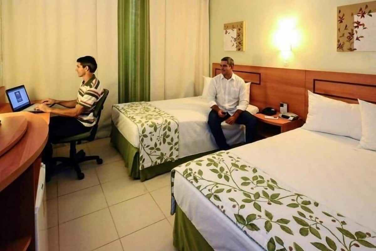 A hotel room with two beds, a desk, and a laptop.
