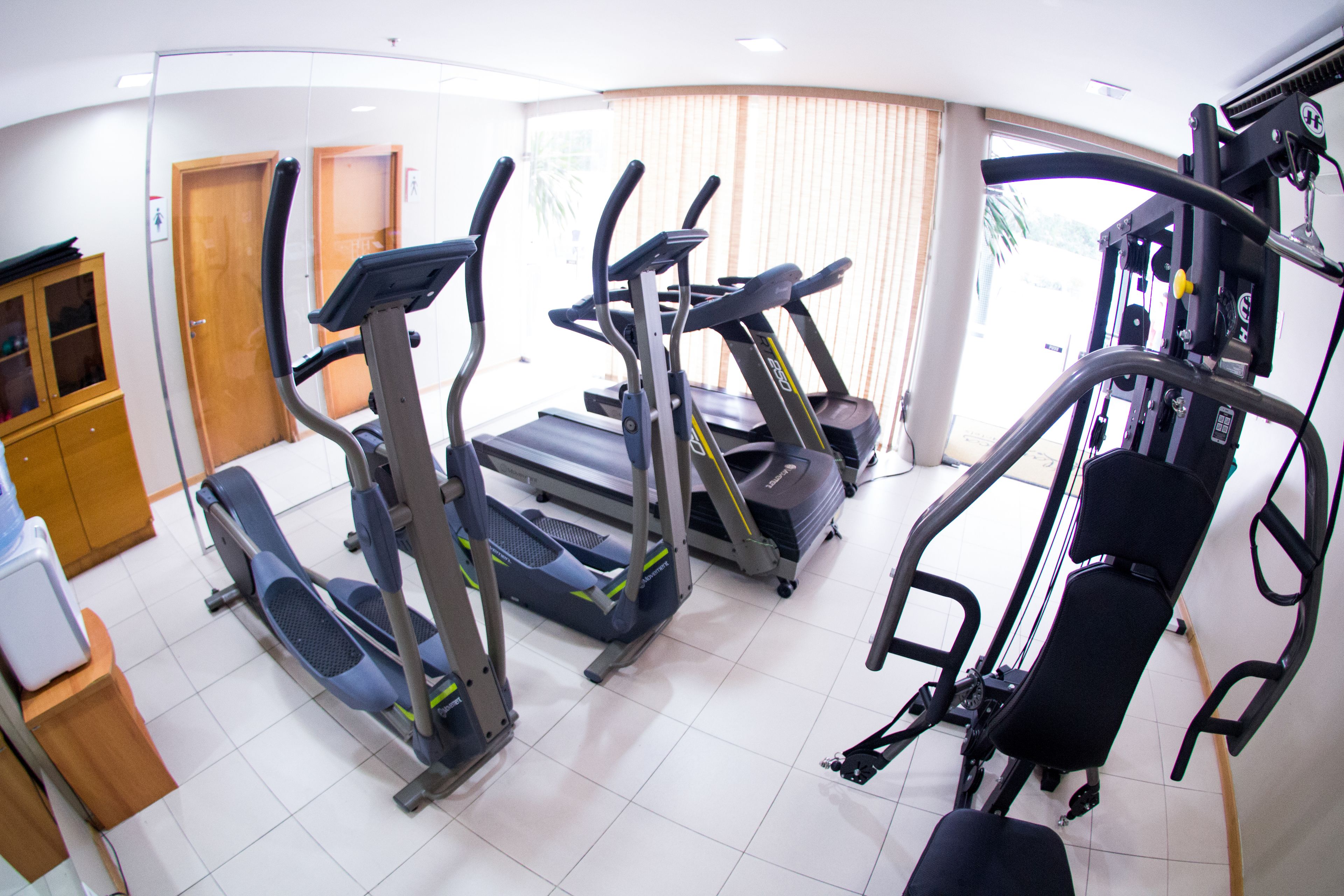 Ein Fitnessraum mit Laufbändern, Crosstrainern und einer Gewichtshantelbank.