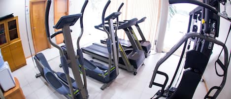 Ein Fitnessraum mit Laufbändern, Crosstrainern und einer Gewichtshantelbank.