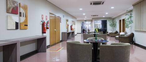 A hotel lobby with a reception desk, seating area, and fire extinguishers on the wall.