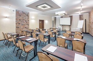 A conference room with multiple tables and chairs, a projector screen, and a brick accent wall.