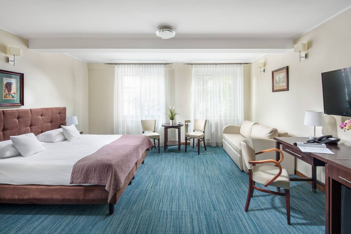 Habitación de hotel con una cama grande, un escritorio con silla, una pequeña mesa con sillas y una televisión.