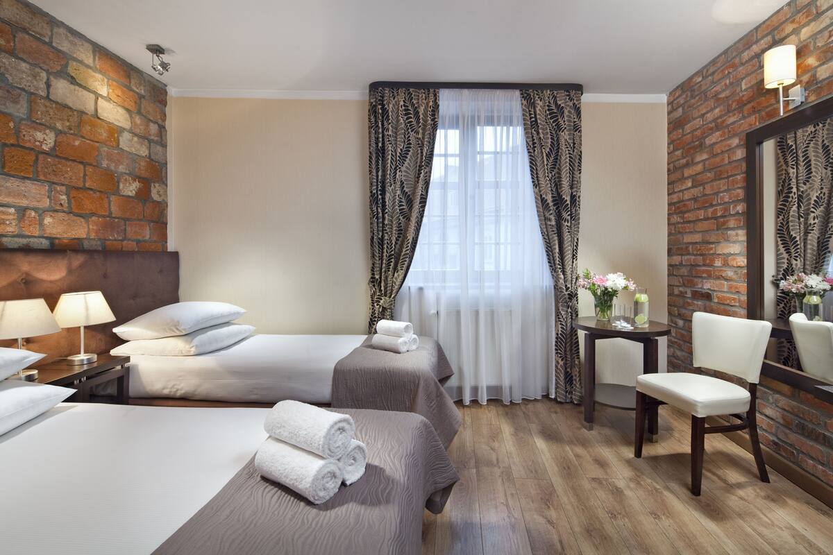 Habitación de hotel con dos camas, una silla, una mesita y un espejo.