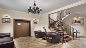 A lobby with a conference room, a staircase, leather seating, and a chandelier. - Hotel Bonum (Gdansk)