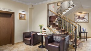 A lobby with leather sofas, a staircase, and a wall-mounted sign. - Hotel Bonum (Gdansk)