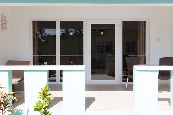Un espacio exterior moderno con un ventanal de vidrio que da a un porche cubierto, una mesa blanca y una silla.