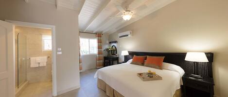 A hotel room with a large bed, a bedside table with a lamp, a glass shower enclosure, and a view of the bathroom.