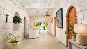 Un couloir avec un comptoir d’accueil, des plantes en pot et un ventilateur de plafond.