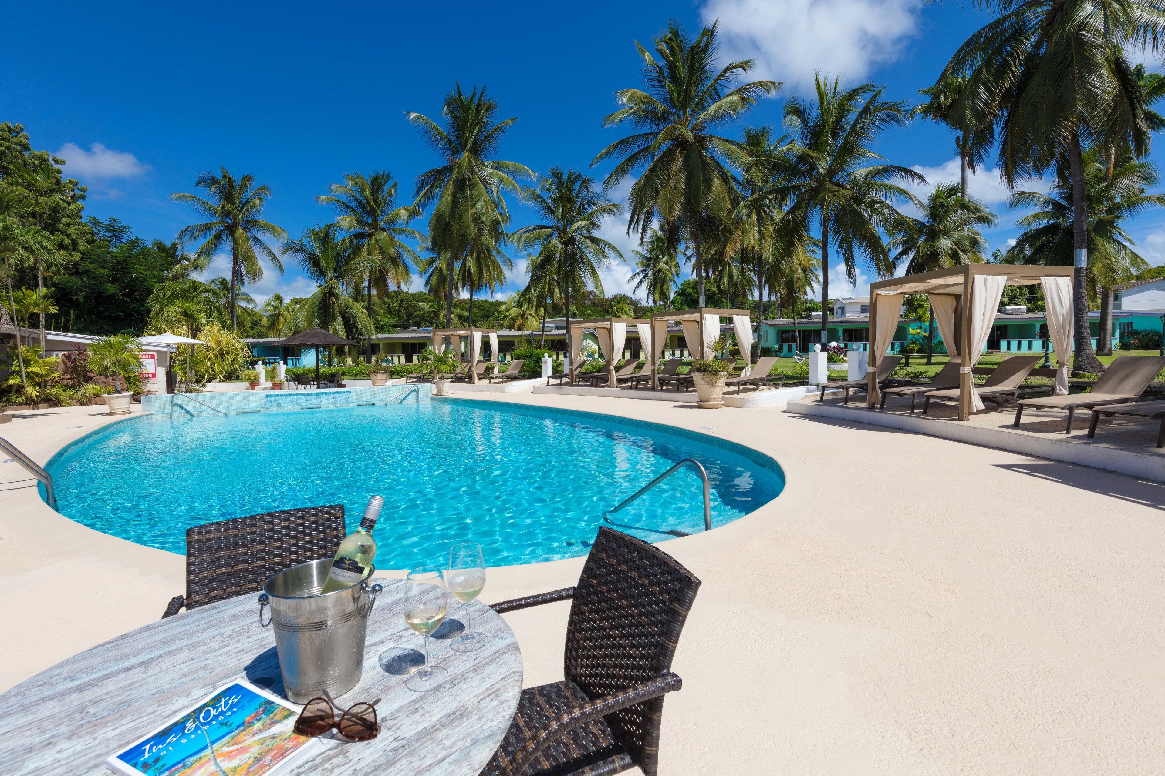 A poolside area with a clear blue pool, lounge chairs, and palm trees.