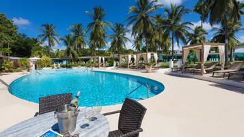 A poolside area with a clear blue pool, lounge chairs, and palm trees.