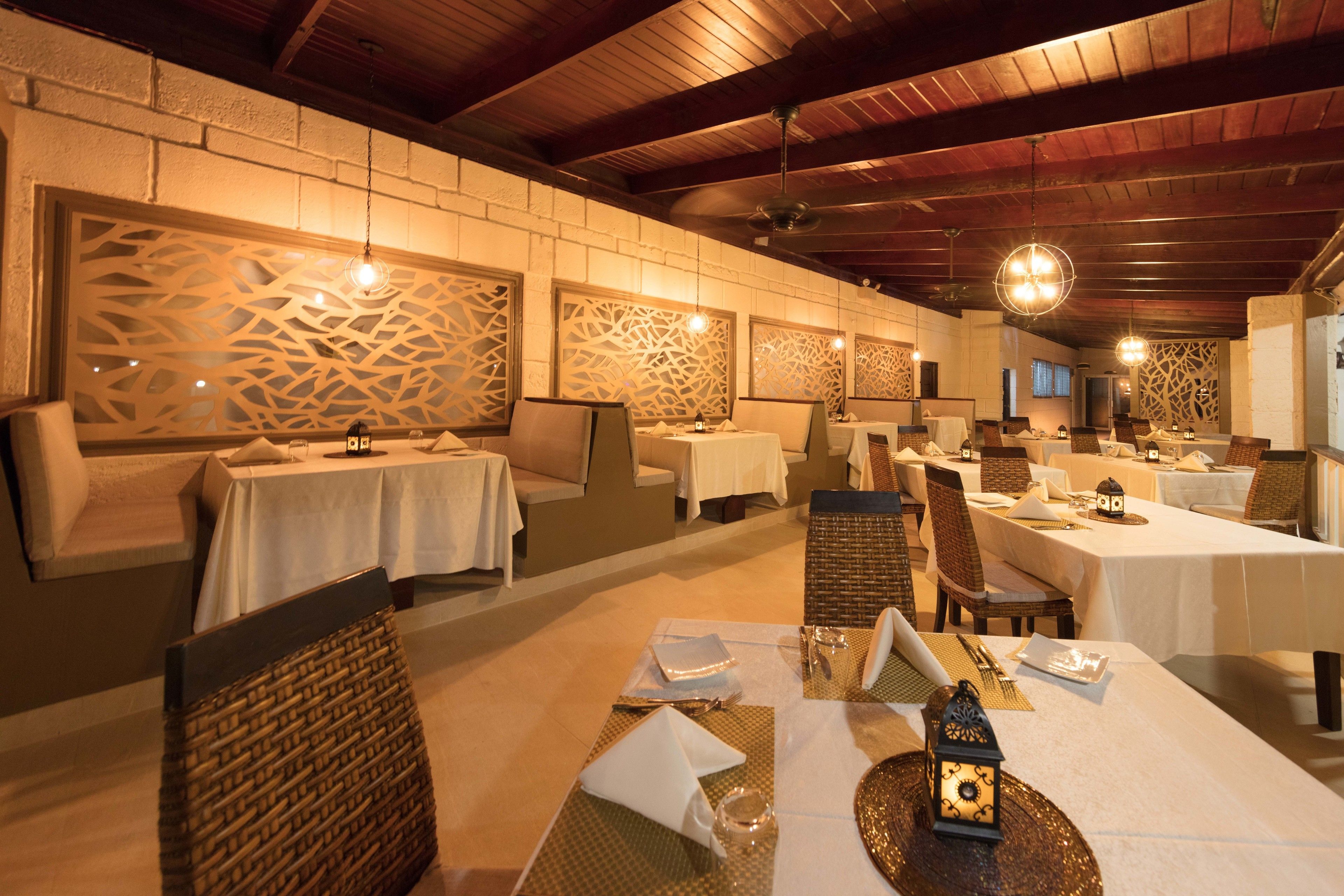 A restaurant with tables set for dining, featuring a brick wall with decorative panels and a wooden ceiling.